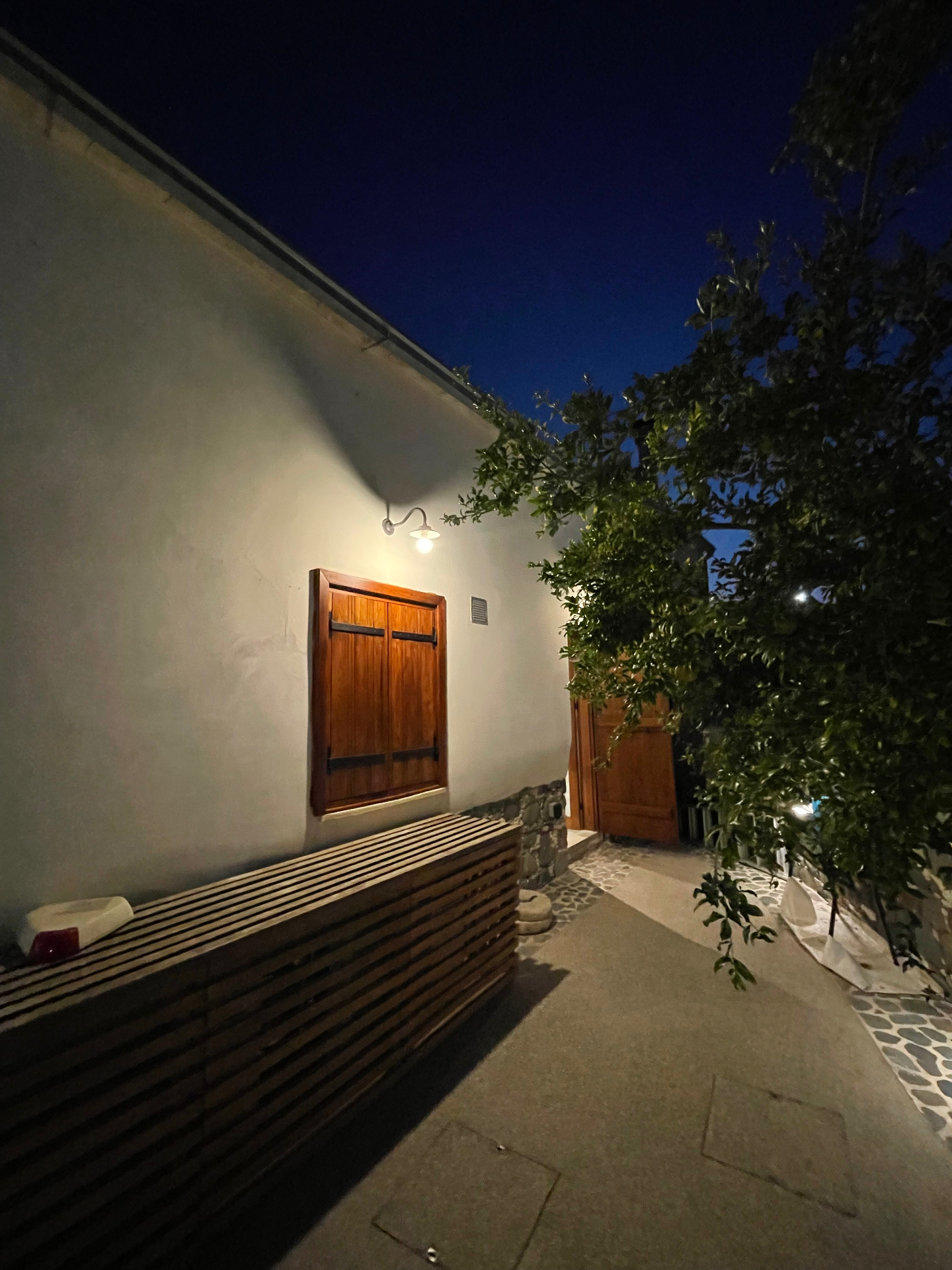 The lantern-lit path beside the shuttered window and citrus tree