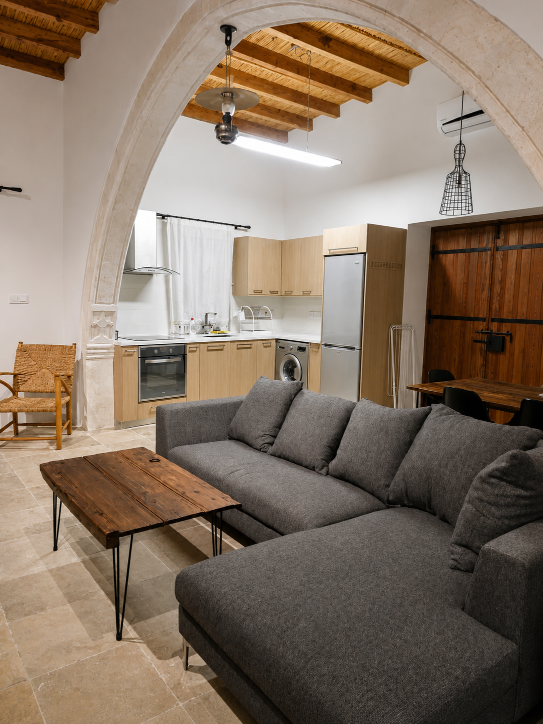 The open-plan living room with grey sofa beneath the timber ceiling
